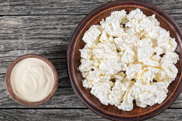 Fiocchi di latte su piatto di argilla, crema aspra in piccola boccia — Foto Stock