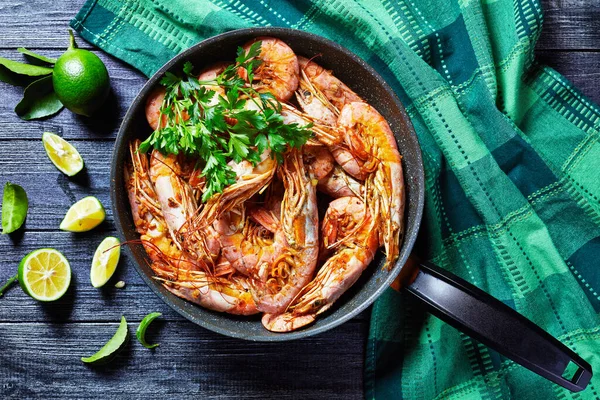 Garlic butter shrimps cooked on a skillet with lime and fresh parsley of big size shrimps or prawns served on a wooden background, top view, close-up