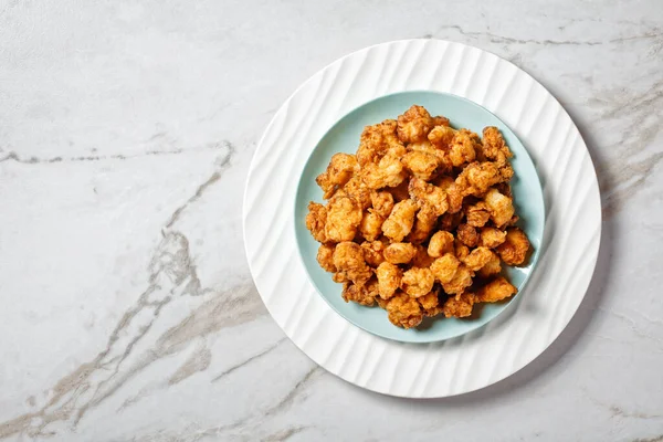 American popcorn chicken of bite-sized chicken breast pieces breaded and fried served on a white plate on a white marble stone background, top view, close-up, free space for the text