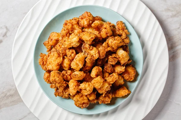 Popcorn chicken - american fast food dish of bite-sized chicken pieces breaded and fried, served on a white plate with ketchup and golden fork on a white marble stone background, top view, close-up