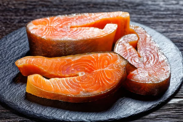 Slices of cold-smoked arctic char on a round slate on a dark wooden background, top view, close-up — Stock Image Slices Cold Smoked Arctic Char Slate Dark Wooden Background Top Royalty Free Stock Photos