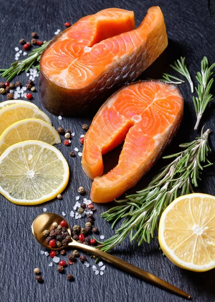 Smoked arctic char steaks on a round cutting board on a dark slate background with lemon, fresh rosemary, peppercorns, top view, close-up — Stock Image Smoked Arctic Char Steaks Cutting Board Dark Slate Background Lemon Stock Picture