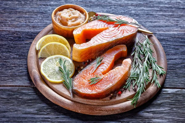 Smoked arctic char steaks on a round cutting board on a dark wooden background with cod roe, lemon, fresh rosemary, peppercorn, top view, close-up — Stock Image Smoked Arctic Char Steaks Cutting Board Dark Wooden Background Cod Royalty Free Stock Images
