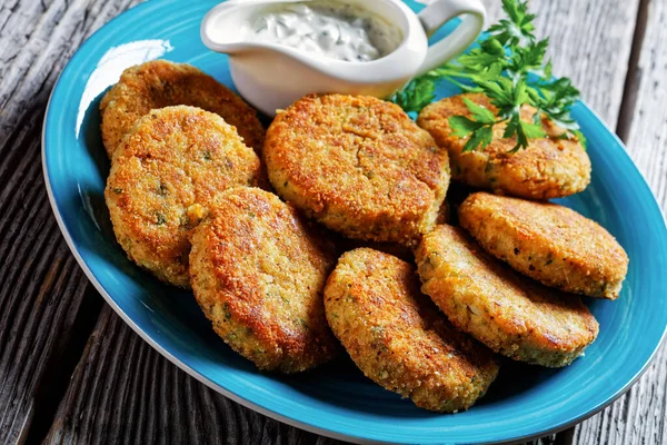 Easy fish cakes of white fish fillet: cod or haddock with potato and parsley, breaded in breadcrumbs served on a plate with tartar sauce in a gravy boat on a wooden background,  top view, close-up