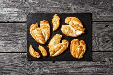 flattened Roast Chicken breasts on a stone tray on a wooden table, horizontal view from above, flat lay, free space clipart