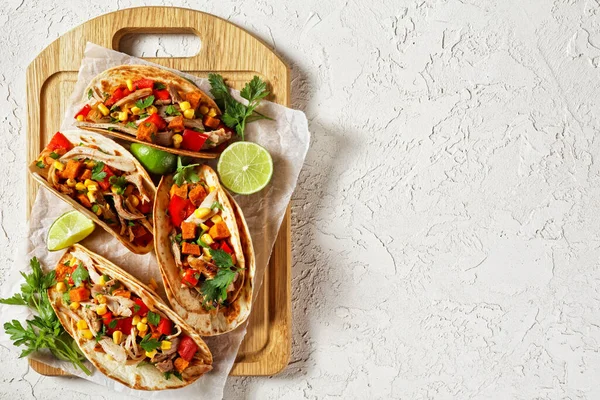 tacos with grilled chicken meat, corn, roasted sweet potatoes cubes, red pepper  and parsley served  on a wooden board on  a white concrete table, flat lay, free space