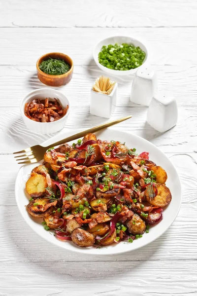 Bratkartoffelsalat 赤玉ねぎとベーコンとローストポテトサラダ木製のテーブルの上に白いプレート 垂直方向のビュー ドイツ料理 — ストック写真