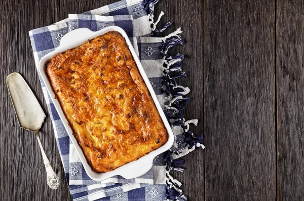 savory potato kugel, baked pudding or casserole of grated potato in a baking dish on a wooden table, jewish holiday recipe, flat lay, free space