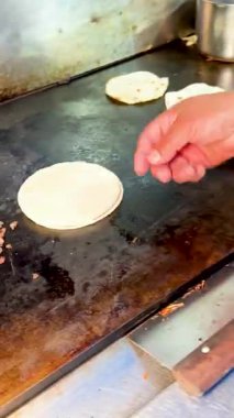 Küçük tortillaları çeviren bir insan, ızgarada pişen, doğranmış etin yanında, taco hazırlığının bir parçası..