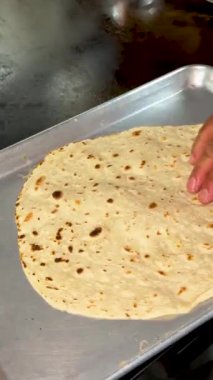 Bir burrito sıcak bir ızgaradan kaldırılıyor ve servis için temiz bir metal tepsiye konuyor..