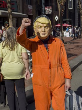 San Francisco, Kaliforniya ABD; 10.18.2025: Bir protestocu Donald Trump maskesi takıyor ve turuncu tulum giyiyor, direnişi simgelemek ve hapishaneyi taklit etmek için yumruk kaldırıyor.