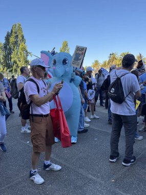 San Francisco, Kaliforniya ABD; 10.18.2025: SanFrancisco 'daki NoKings mitinginde bir katılımcı telefon ve kırmızı çanta tutarken tam boy bir mavi fil kostümü giyer..