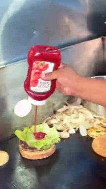 Marul ve ketçaplı hamburger, sotelenmiş soğan ve çöreğin yanında sıcak bir ızgaranın üzerinde oturur. Fast food hazırlığı devam ediyor.