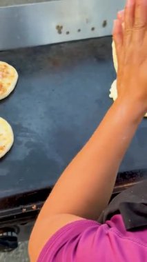 Kalkmış bir el, un kaplı, ızgara üzerinde pişirme işlemi sırasında jestler, arka planda iki pupusas kahverengisi.