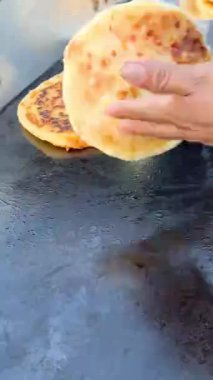 Bir aşçı, sokak yemeklerinin hazırlanması sırasında esmerleşmesini sağlamak ve geleneksel teknikleri sergilemek için tavada bir pupusa çevirir..