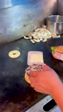 Dolu bir mutfakta dilimlenmiş soğan ve sandviç malzemeleriyle çevrili jambonlu burger ve etli börek de dahil olmak üzere birden fazla hamburger gösteren ızgara..