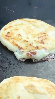 Eridikçe uzayan peynirli ızgara bir pupusa, siyah bir ızgaranın tepesinde yapışkanlıkla yakalanır. Rahat sokak yemeklerinin ikonik görüntüsü.