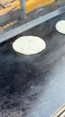 Yeni oluşmuş bir pupusa düz bir tavada pişmeye başlar, buhar yükselir ve yumuşak hamur kahverengileşmeye hazırdır. Hazırlığın ilk aşaması.