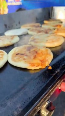 Sıcak bir ızgarada aynı anda yemek pişiren, buhar çıkaran ve kalabalık bir sokak yiyecek ortamında altın kabuklar oluşturan birkaç pupusa..