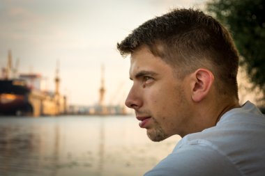 Arka planda bir gemiyle nehir kıyısında oturan genç adam Başkanı