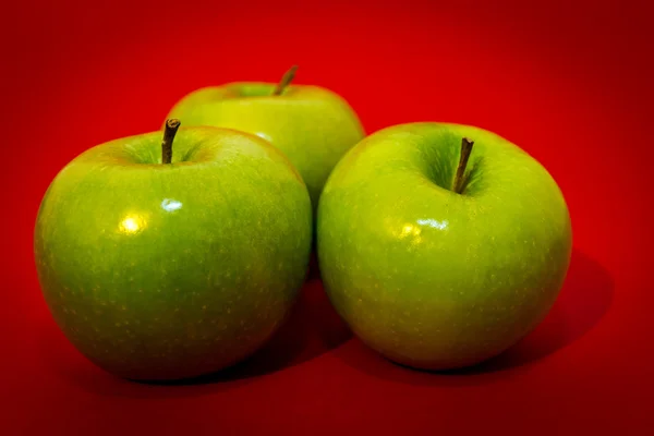 Three green apples on the red background — Stock Photo, Image