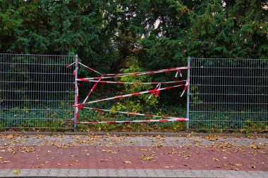 Yeşil Ağaçlar ve Düşen Sonbahar Yaprakları Arasında Kırmızı ve Beyaz Alarm Şeridine Sarılı Metal Çitler