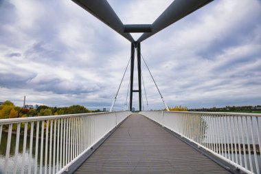 Ren Nehri üzerindeki boş yaya köprüsü Sonbahar Ağaçları ve Dsseldorf Almanya 'sında Bulutlu Gökyüzü Altındaki Uzak Şehir manzarası