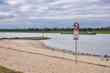 Dsseldorf Almanya 'sında Kargo Mavnası Ren Nehri ve Bulutlu Gökyüzü Altında Kırmızı İşaretli Sandy Shore' da Yüzme Yok tabelası