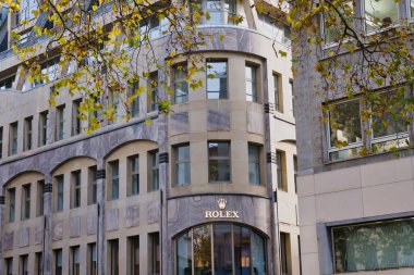 A stunning architectural building featuring a luxury watch brand, surrounded by golden autumn leaves.
