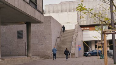Two people walk towards a set of stairs leading to an upper area while a lone figure ascends.