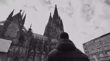 Köln, Almanya, 12.12.2025 - Aşağıdaki Majestic Köln Katedrali Kışlık Ceketli Turistle Göründü Siyah ve Beyaz Video Görüntülerinde Gökyüzüne Karşı Gotik Kuleler