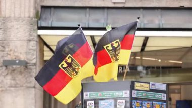 Federal kartal sembollü Alman ulusal bayrakları bir alışveriş bölgesindeki bir sokak hediyelik eşya standına el sallıyor. Kentsel bir ortamda Almanya 'yı temsil eden siyah kırmızı ve altın bayrakların yakın görüntüsü.