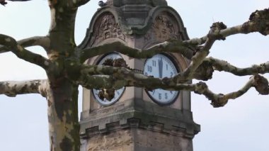 Tarihi taş saat kulesi kısmen bir Avrupa şehrindeki çıplak ağaç dalları tarafından çerçevelenmiş. Şehir ortamında klasik tasarım ve analog saat yüzlerine sahip mimari yapı simgesi.