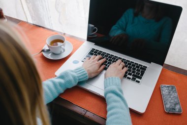 Woman typing on keyboard of a laptop with a coffee cup on table.