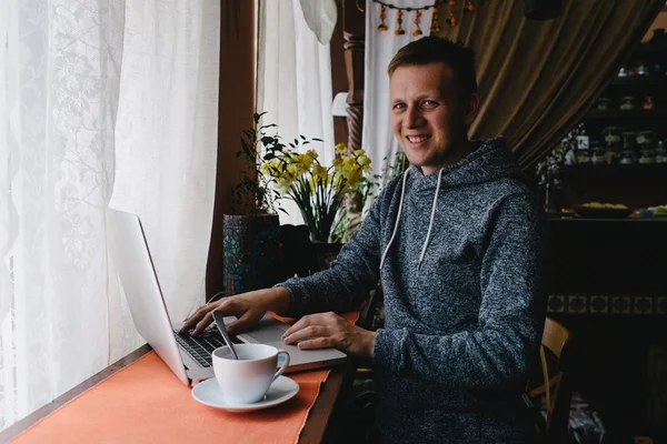 Un hombre usando un portátil y un teléfono celular en un café. Joven bebiendo c — Foto de Stock