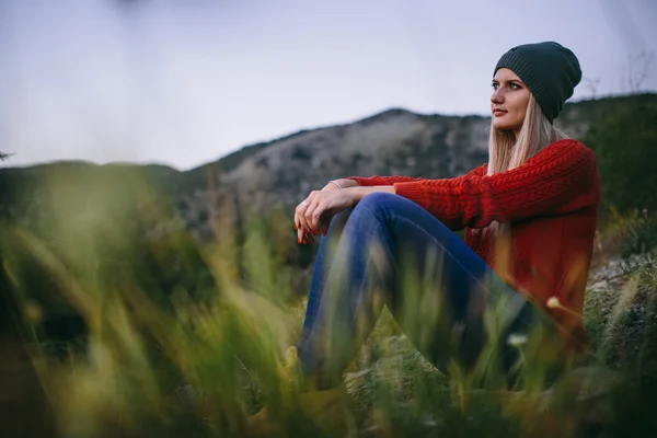 Portrait of a beautiful young blonde woman sits outdoor on the background of mountain — Stock Photo, Image