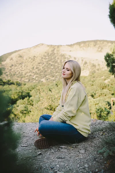 Jeune femme blonde assise en plein air sur un fond de montagnes — Photo