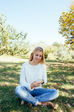 young woman sitting in the park and using her cell phone. woman sending a text message from her mobile phone outdoor