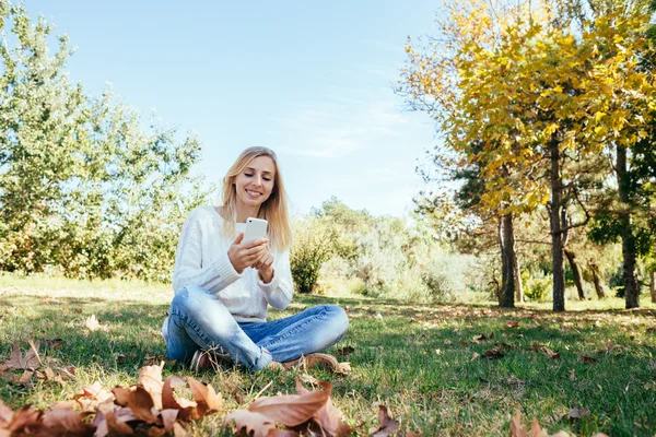 Junge Frau, die im Park sitzt und ihr Handy benutzt. Frau schickt SMS vom Handy ins Freie — Stockfoto