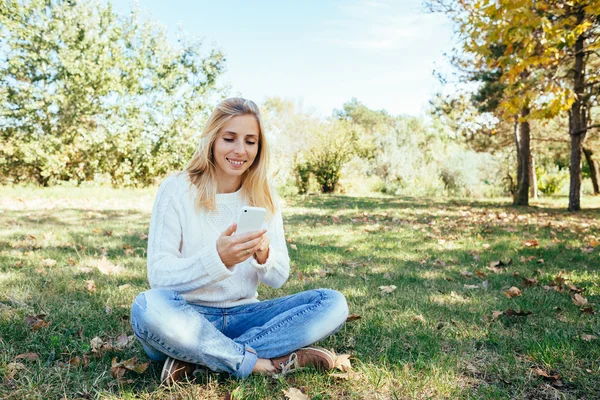 Junge Frau, die im Park sitzt und ihr Handy benutzt. Frau schickt SMS vom Handy ins Freie — Stockfoto