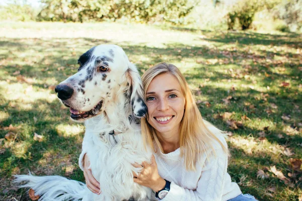 Feliz jovem mulher abraçando um grande cão branco no parque — Fotografia de Stock