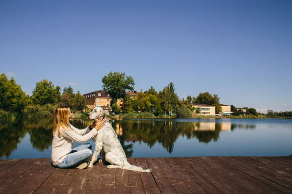 Happy young woman hugging a big white dog on a wooden bridge on the background of the lake — Stock Photo, Image