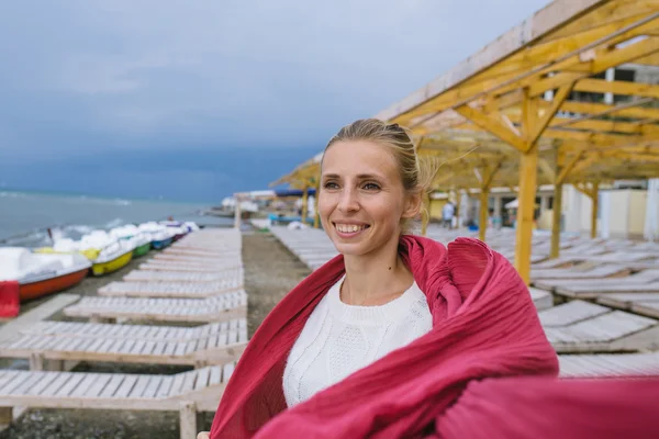 Young woman wrapped up in a red woven scarf by the sea — Zdjęcie stockowe