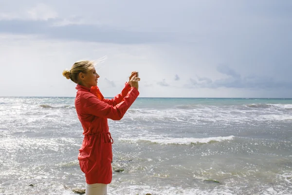 Young woman use mobile phone taking photo on the background stormy sea — Zdjęcie stockowe