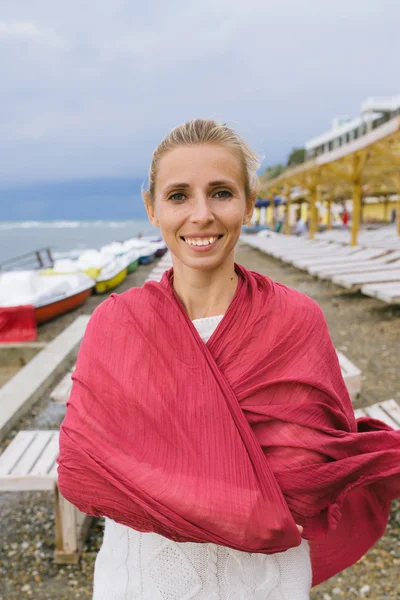 Young woman wrapped up in a red woven scarf by the sea — Zdjęcie stockowe