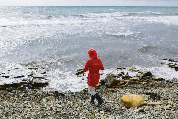 Jeune femme dans un imperméable rouge et caoutchouc bleu venant à la ligne d'eau de mer — Photo