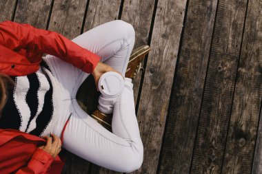 ahşap zemin üzerinde çapraz bacaklı oturan ve bir kahve fincanı tutan genç bir kadın kırpılmış görüntü