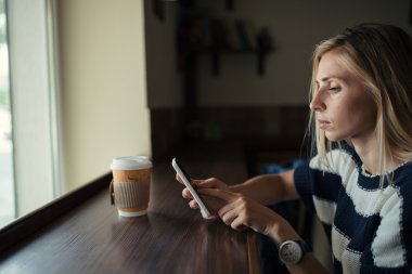 Kafedeki cep telefonundan mesaj atan genç bir kadın. Ahşap masada akıllı telefon kullanan bir kadın.