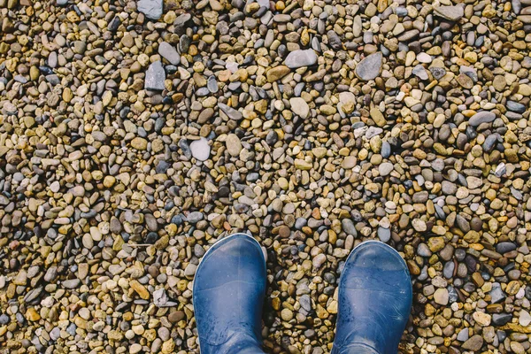 Ženské nohy v tmavě modré gumové boty stojící na mokrý štěrk — Stock fotografie