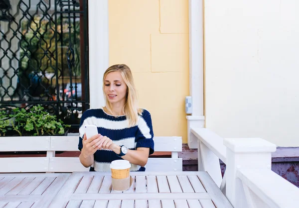 Eine junge Frau schickt im Café eine SMS von ihrem Handy. Frau benutzt Smartphone auf Holztisch in Outdoor-Café — Stockfoto